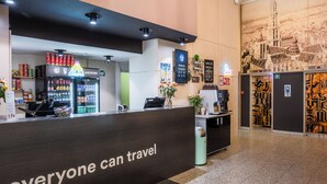 A reception area with a dark reception desk, a beverage cooler, and a wall-mounted menu board. - a&o Antwerpen Centraal (Antwerp)