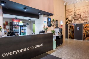Un área de recepción con un mostrador oscuro, un refrigerador para bebidas y un panel de menú en la pared.