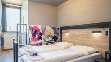 Una habitación de hotel con cama, una mesita y un radiador. Hay carteles en la pared anunciando un evento.