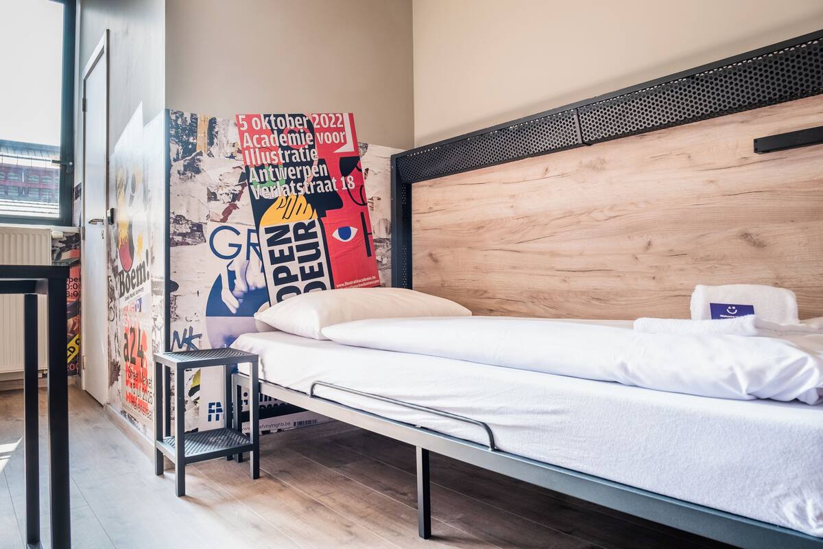 A single bed with a wooden headboard, a small bedside table, and a poster on the wall.