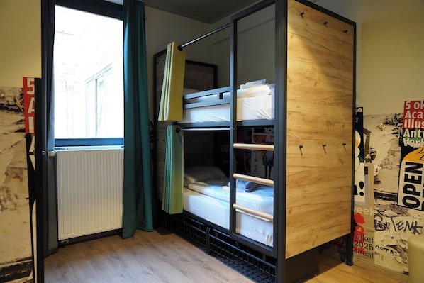 A dorm-style room with bunk beds, a radiator, and a window with curtains. - a&o Antwerpen Centraal (Antwerp)