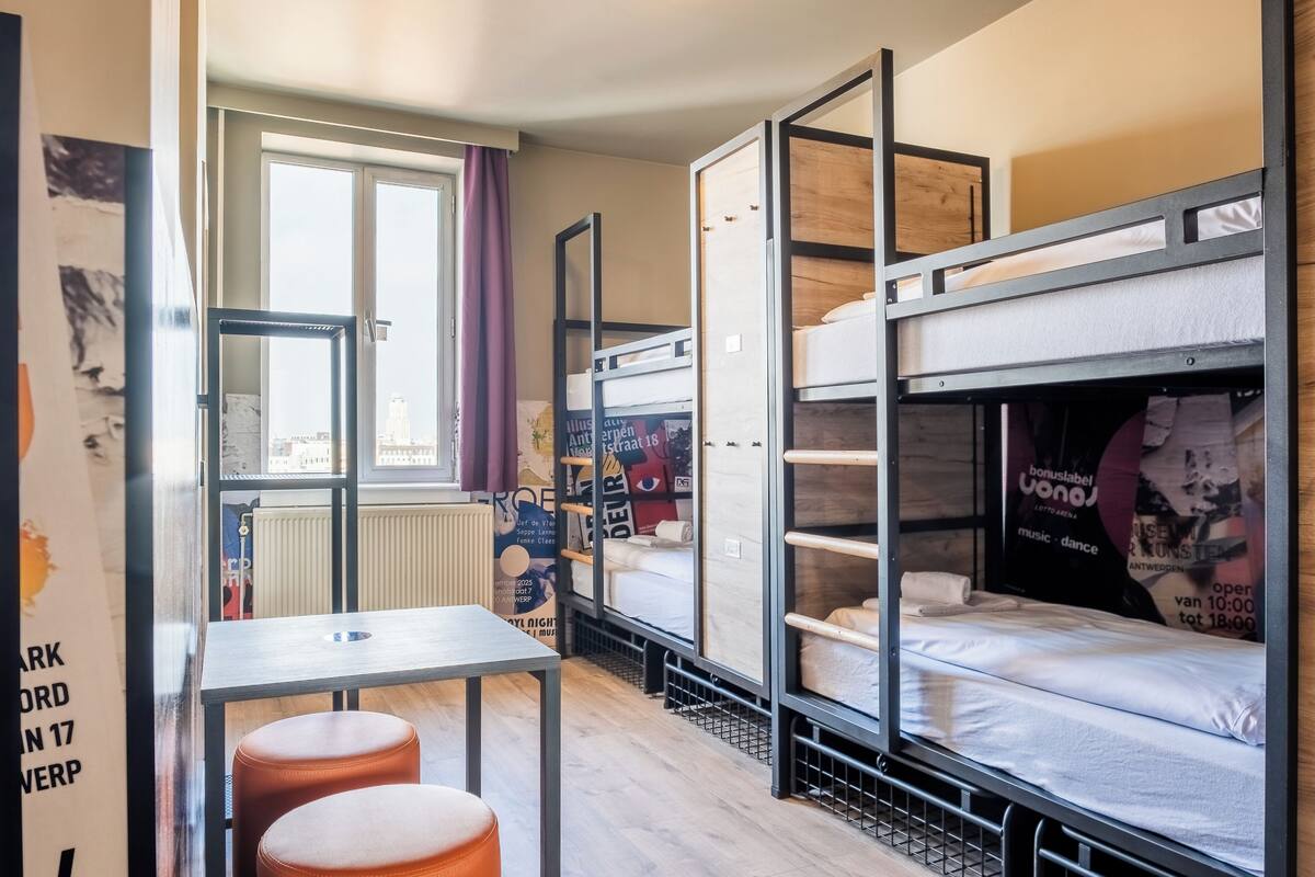 A dormitory room with bunk beds, a table, and a window with curtains.