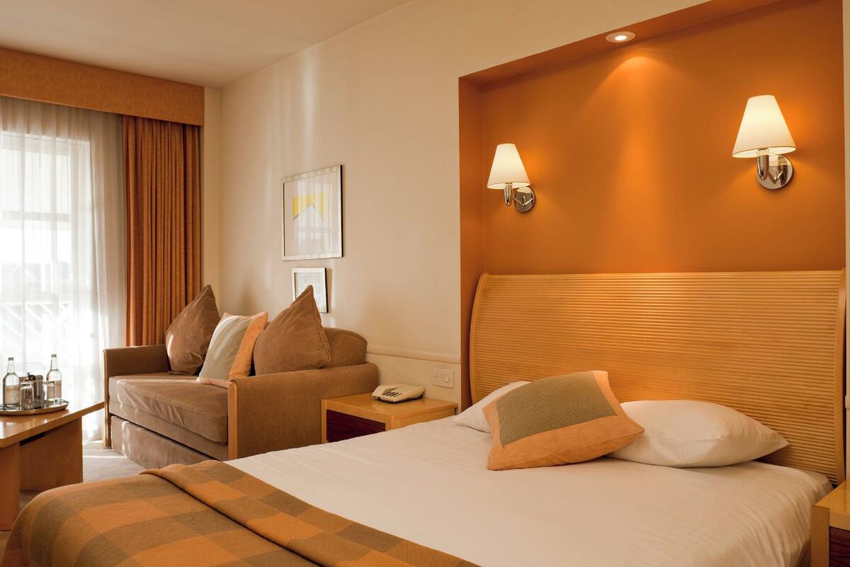 Ein Hotelzimmer mit einem großen Bett, einem Schlafsofa, einem Nachttisch mit Lampe und einem fenster mit Vorhängen.