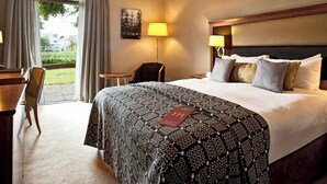 Une chambre d’hôtel avec un grand lit, deux lampes de chevet, un bureau avec une chaise, une petite table et une vue sur l’extérieur.