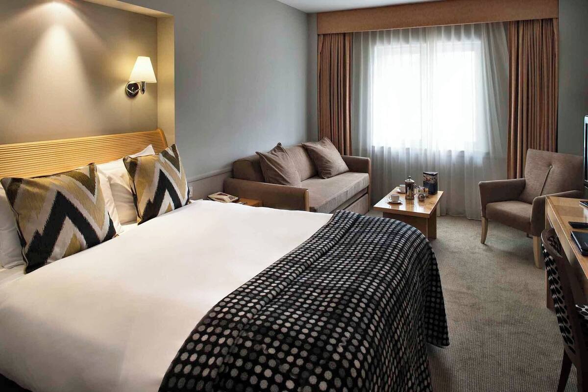 Ein Hotelzimmer mit einem großen Bett, einem Sofa, einem Sessel, einem kleinen Tisch und einem Fernseher.