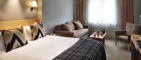 A hotel room with a large bed, a sofa, a chair, a small table, and a TV.