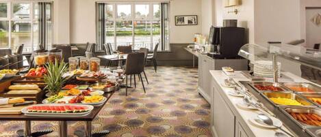 Zona de buffet con diferentes opciones de comida, un televisor y vistas al exterior a través de amplias ventanas.