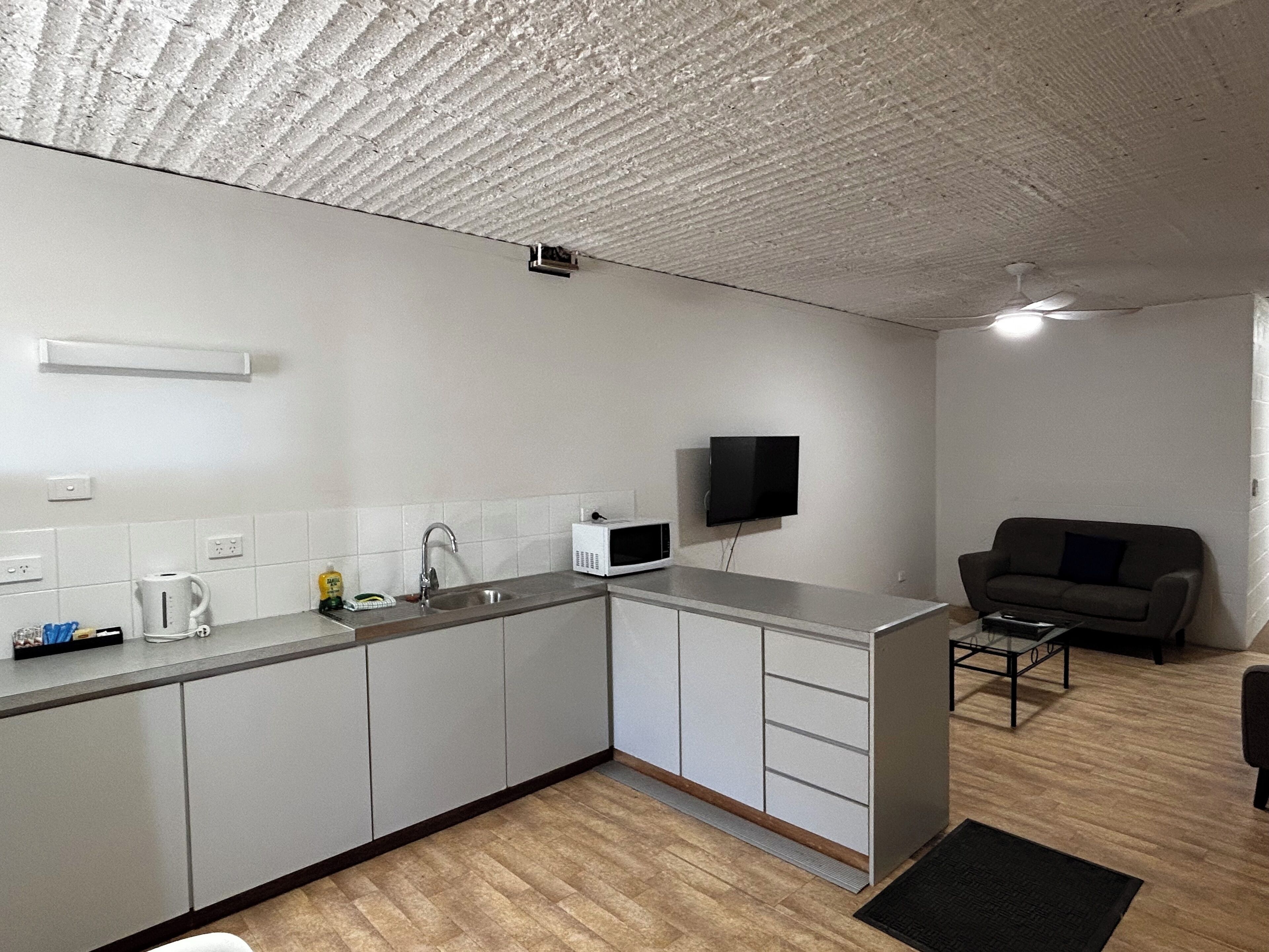 A compact kitchen with a microwave, sink, and a flat-screen TV mounted on the wall.