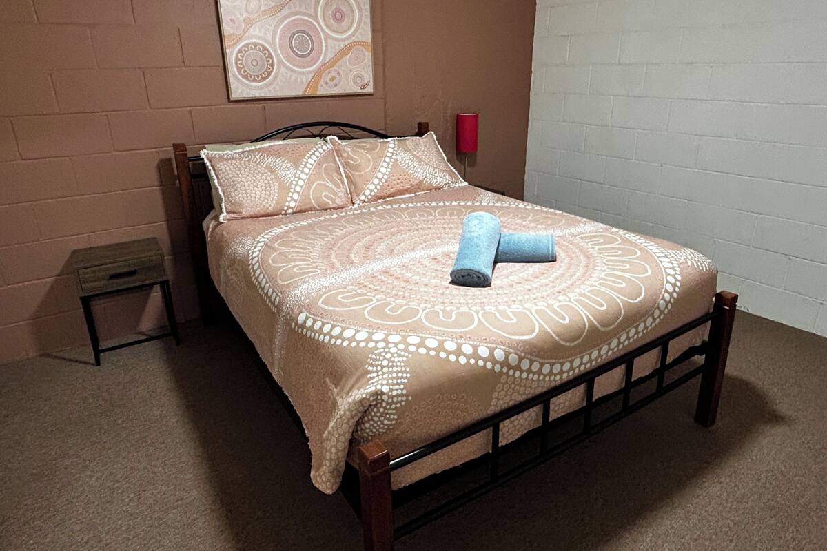 A bed with a patterned bedspread, pillows, and a rolled towel.