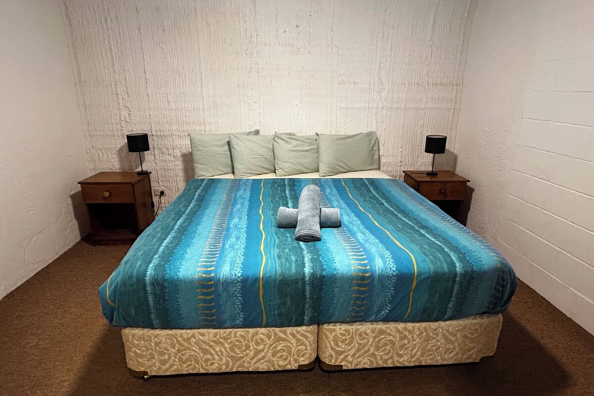 A neatly made bed with a patterned bedspread, two bedside tables with lamps, and a textured wall.