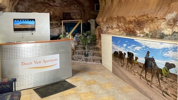 Un intérieur à thème désertique comprenant un comptoir d’accueil, un téléviseur fixé au mur et une fresque représentant des chameaux.