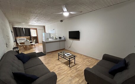 A modern living room with two grey sofas, a coffee table, and a kitchen area with a microwave and TV.