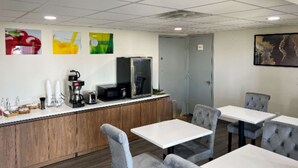 Un café moderno con mostrador de madera, mesas blancas y sillas tapizadas en gris.