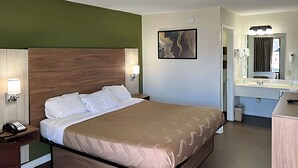 Habitación de hotel con cama, mesita de noche, lámpara y baño con espejo y lavabo.