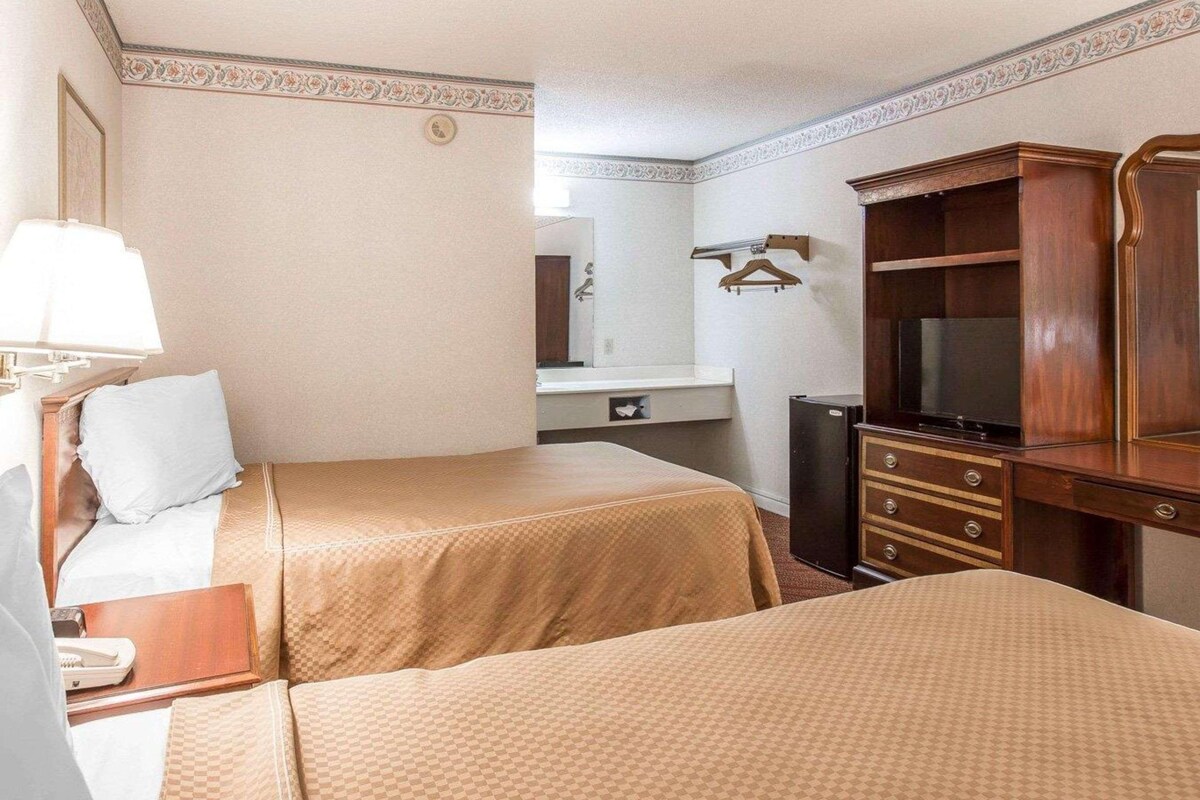 A hotel room with two beds, a TV, a dresser, a mirror, and a bathroom visible in the background.