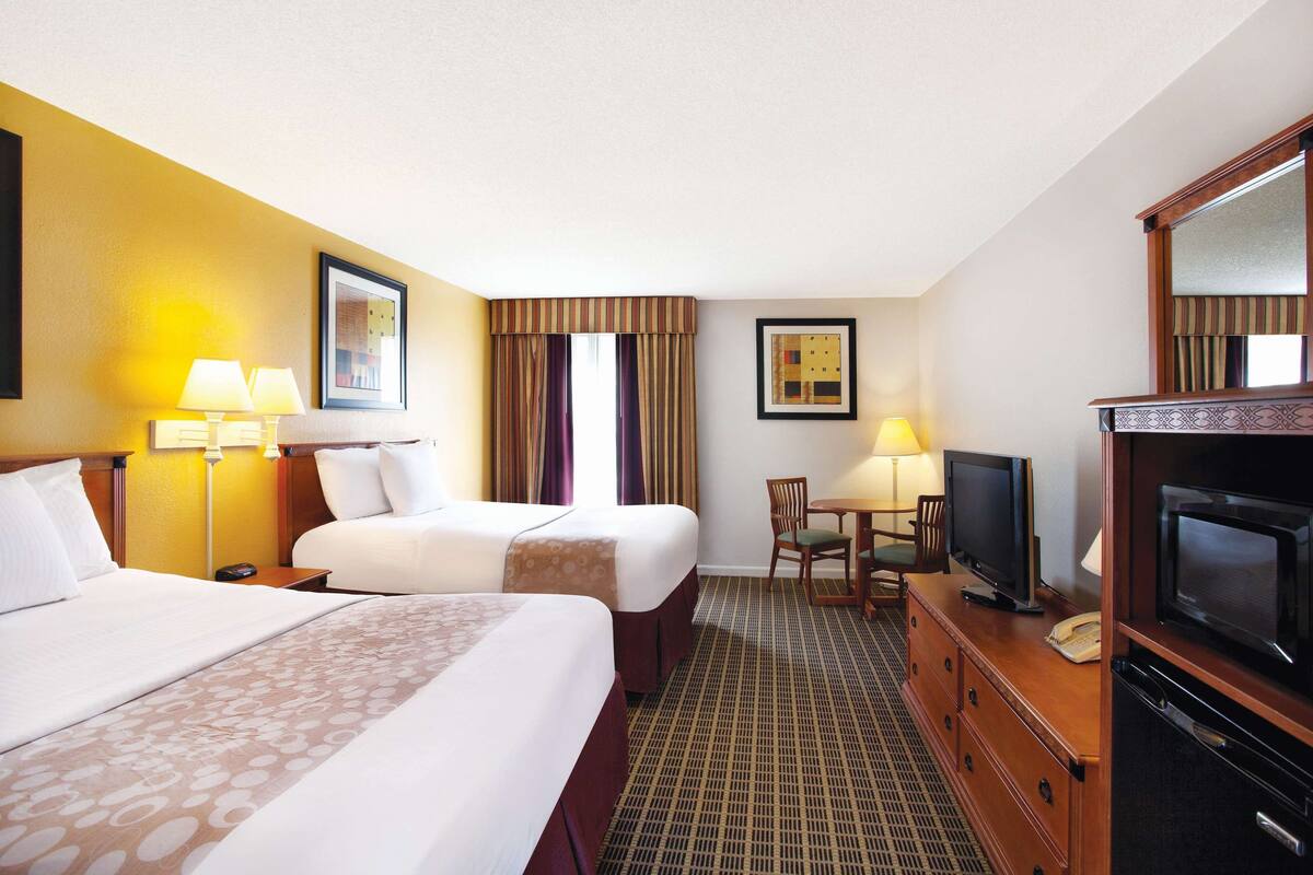 A hotel room with two beds, a desk with a television, a chair, and a dresser.