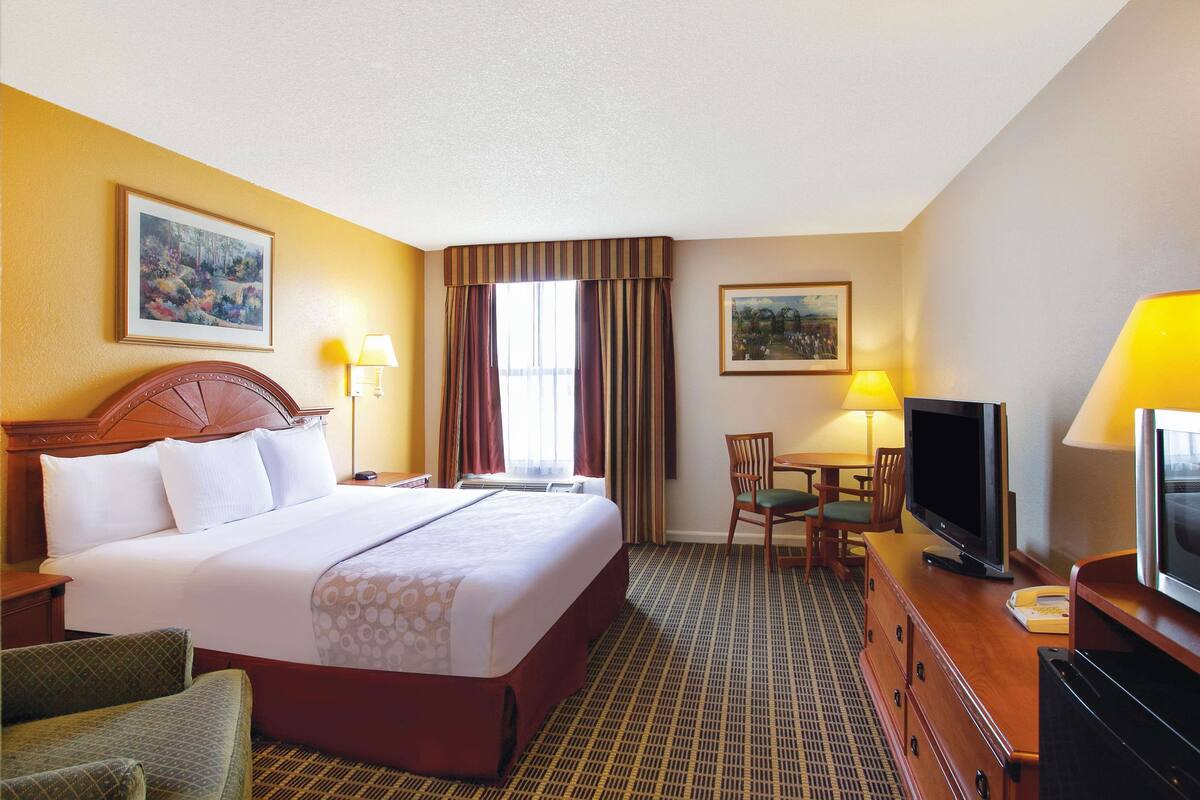 A hotel room with a large bed, a television, a desk with a lamp, and two chairs.
