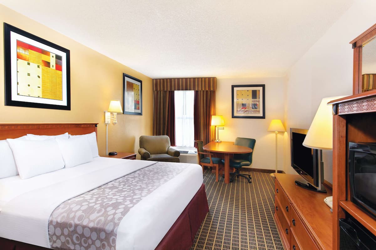 A hotel room with a large bed, a desk with a chair, a television, and two lamps.