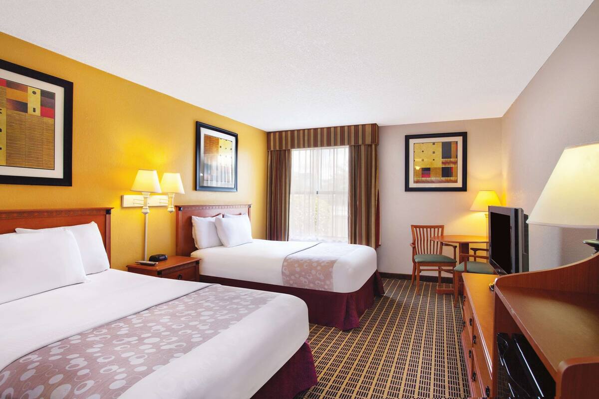 A hotel room with two beds, a desk with a chair, a television, and a window with curtains.