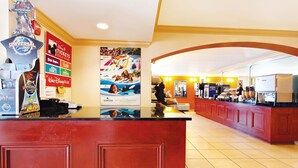 Zona de recepción de un hotel con mostrador, carteles que anuncian Disney World y vistas al comedor.