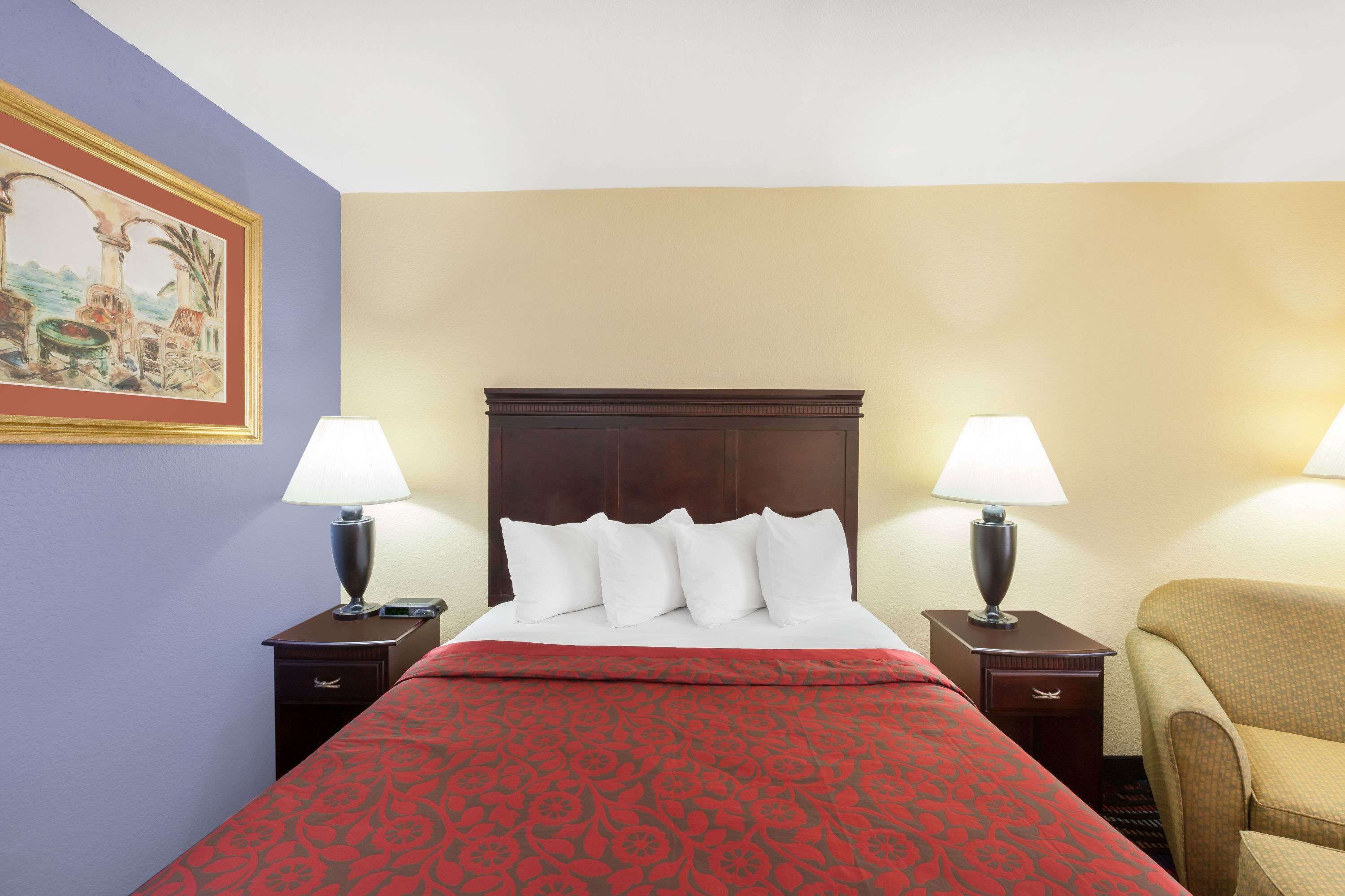 A hotel room with a bed, two nightstands with lamps, a chair, and a painting on the wall.