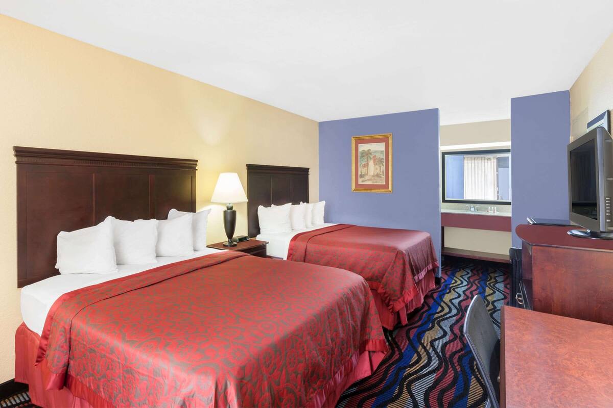 A hotel room with two beds, a TV, a desk, and a window.