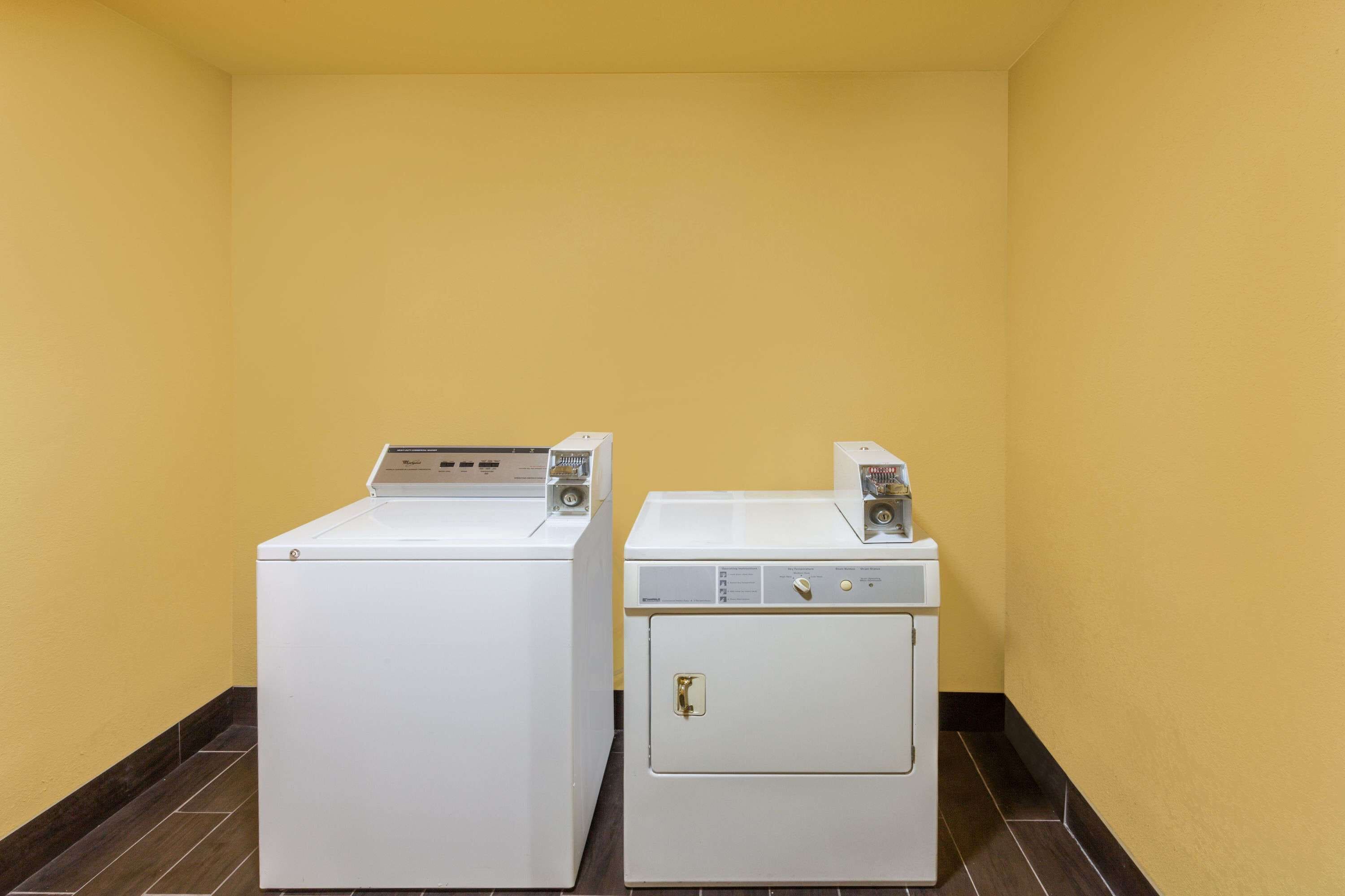 Two white washing machines in a corner with yellow walls and dark floor tiles.