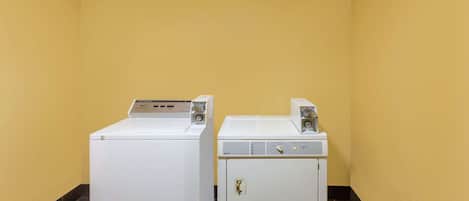 Two white washing machines in a corner with yellow walls and dark floor tiles.