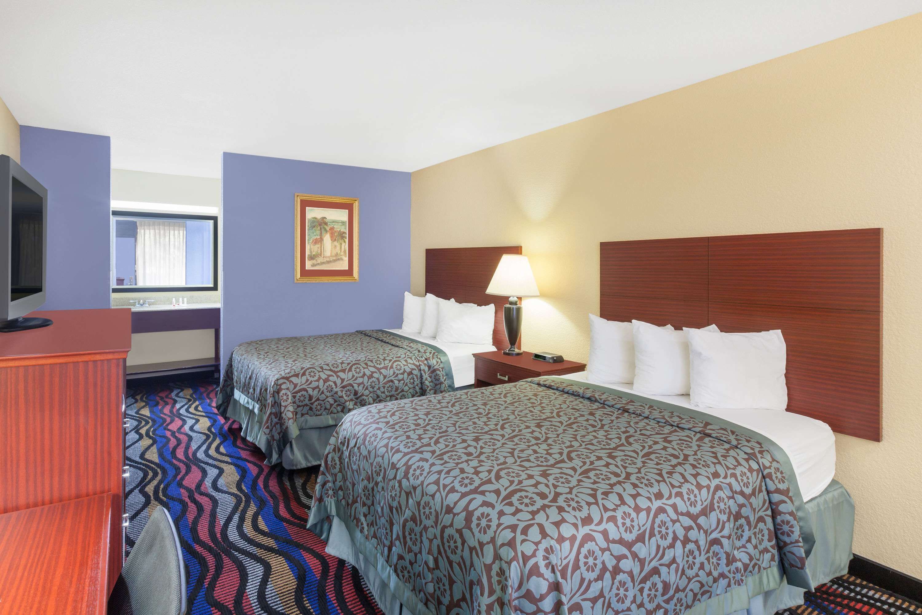 A hotel room with two beds, a desk, a TV, and a window with curtains.