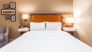 A hotel room with a large bed, two bedside tables with lamps, a chair, and framed pictures on the wall.
