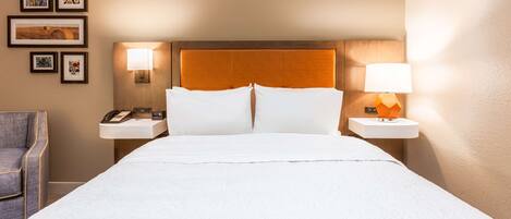 A hotel room with a large bed, two bedside tables with lamps, a chair, and framed pictures on the wall.