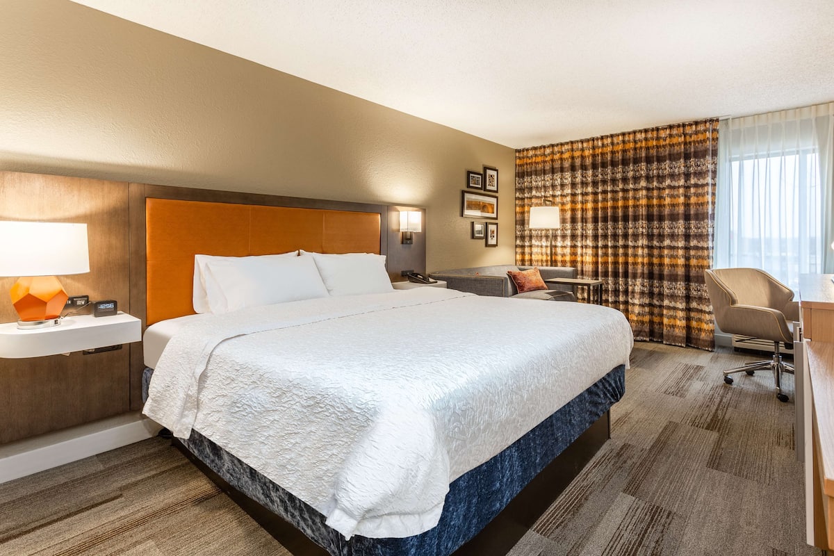 A hotel room with a large bed, a desk, a chair, and a window with curtains.