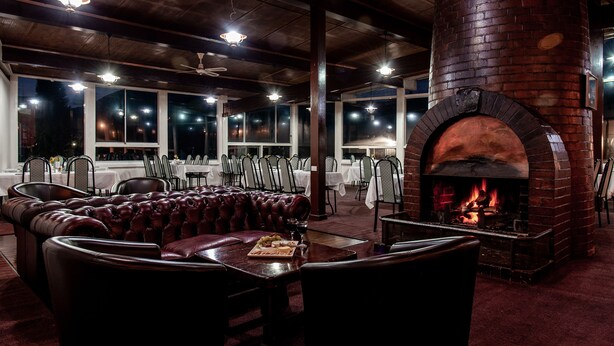 A restaurant with leather seating, a brick fireplace, and tables set for dining. - Silver Hills Motel (Queenstown)