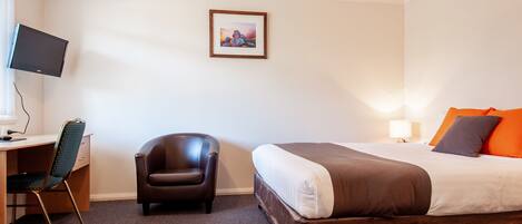 Habitación de hotel con una cama, un escritorio con computadora, una silla y un cuadro en la pared.