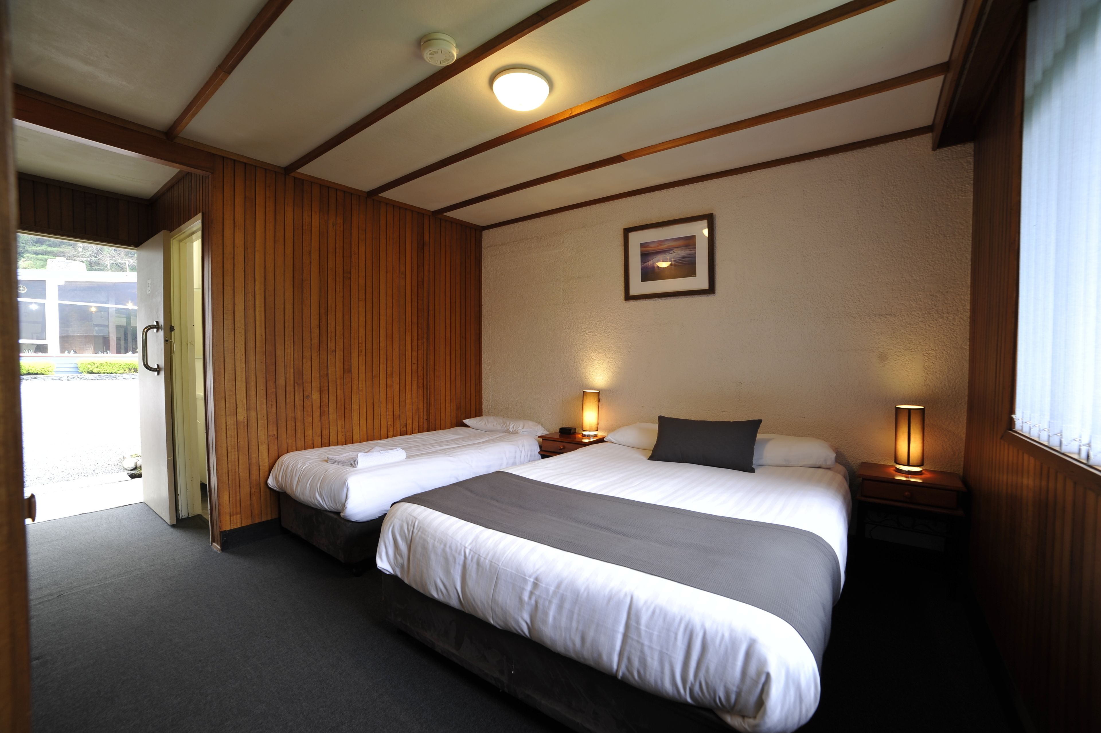 A hotel room with two beds, wooden paneling, a framed picture on the wall, and a window with blinds.