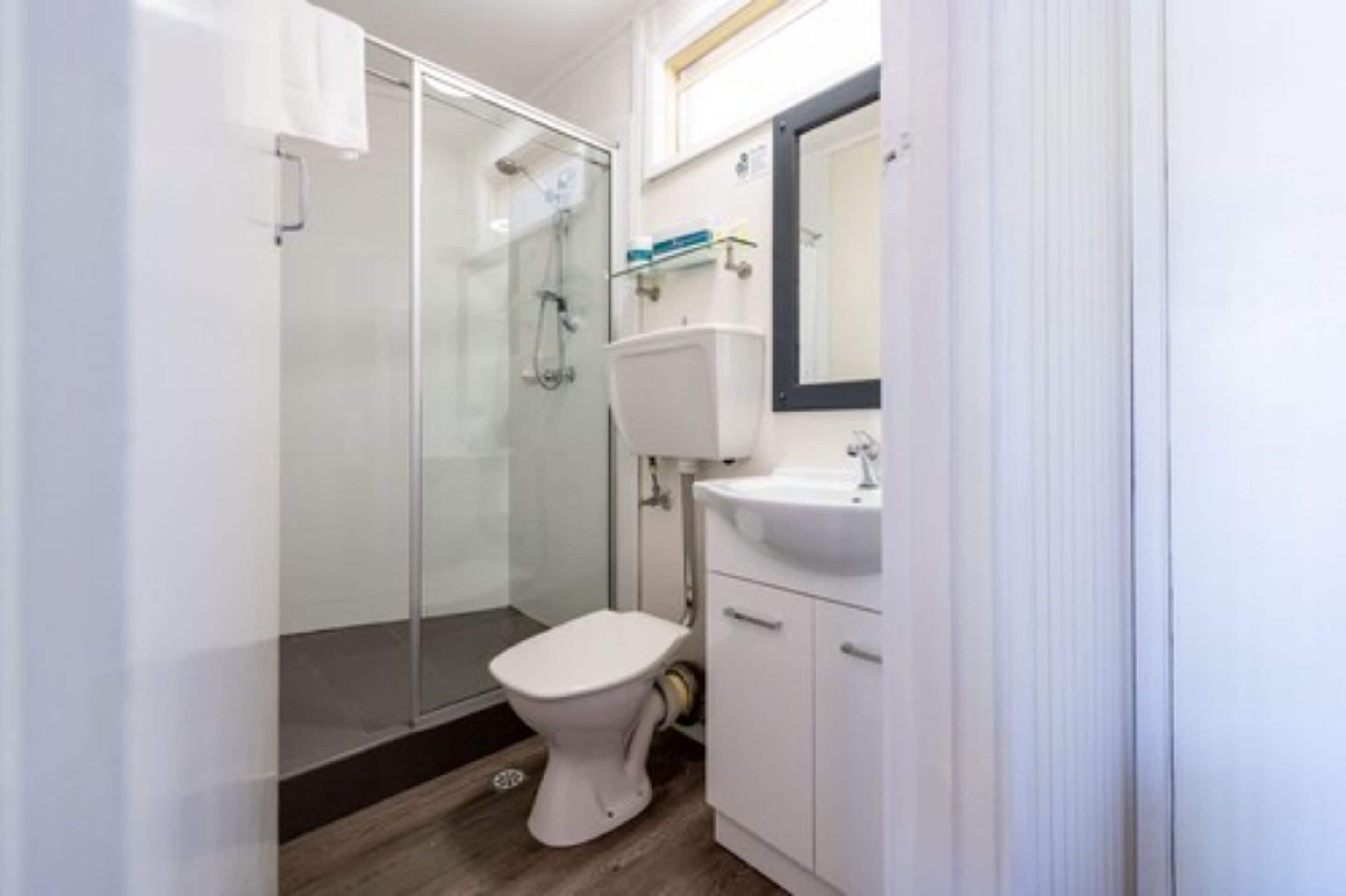Une salle de bain moderne avec une douche à parois de verre, des toilettes blanches et un lavabo surmonté d’un miroir.