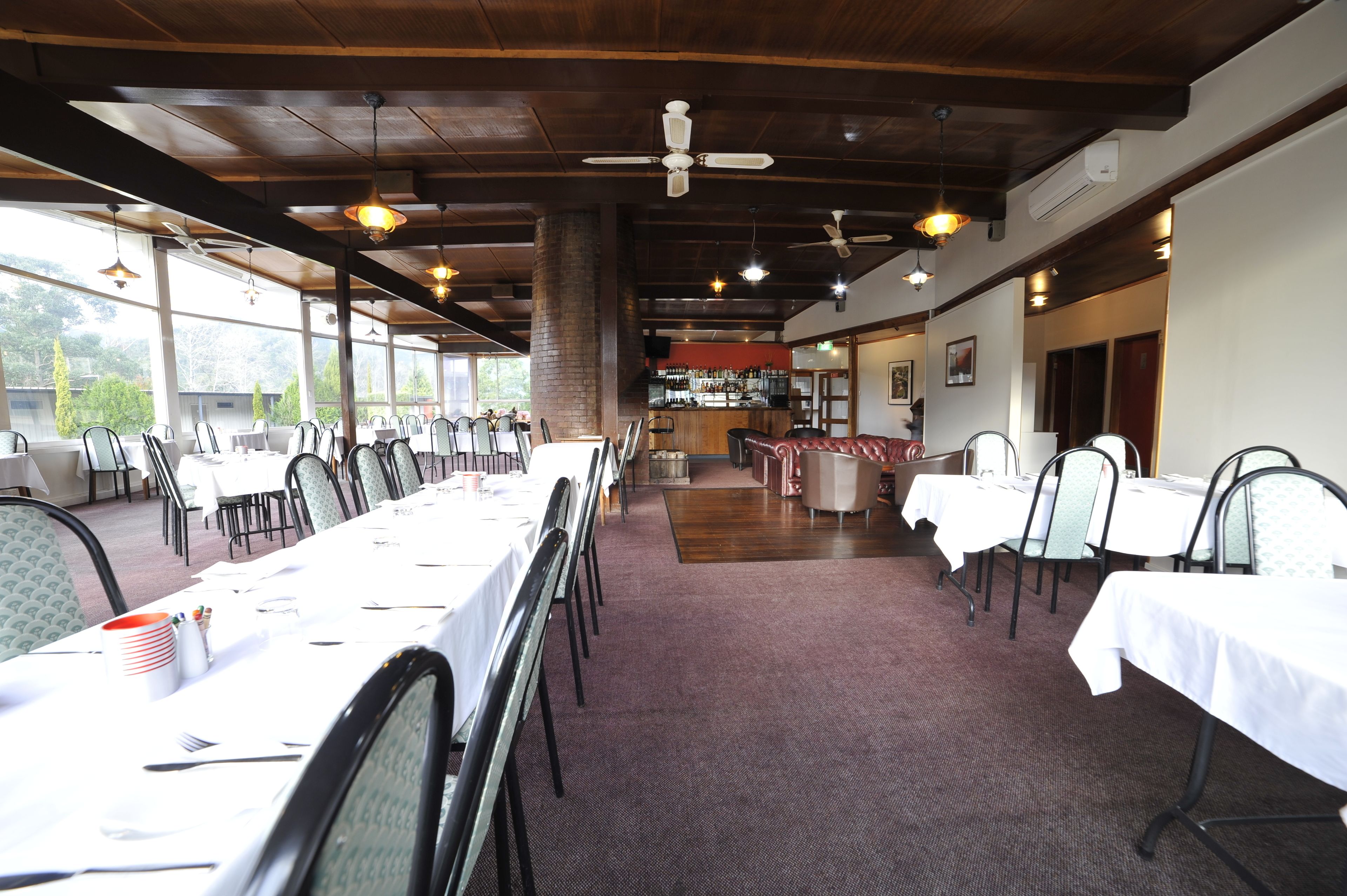 A restaurant with long tables, chairs, and a bar area.