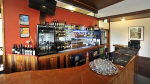 A bar area with a wooden counter, a variety of bottles, a refrigerator, and a tray with glasses. - Silver Hills Motel (Queenstown)