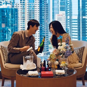 A couple seated on a sofa with a cityscape view, a table with a bottle, glasses, and decorative items. - China World Hotel Beijing A Shangri-La Hotel (Beijing)