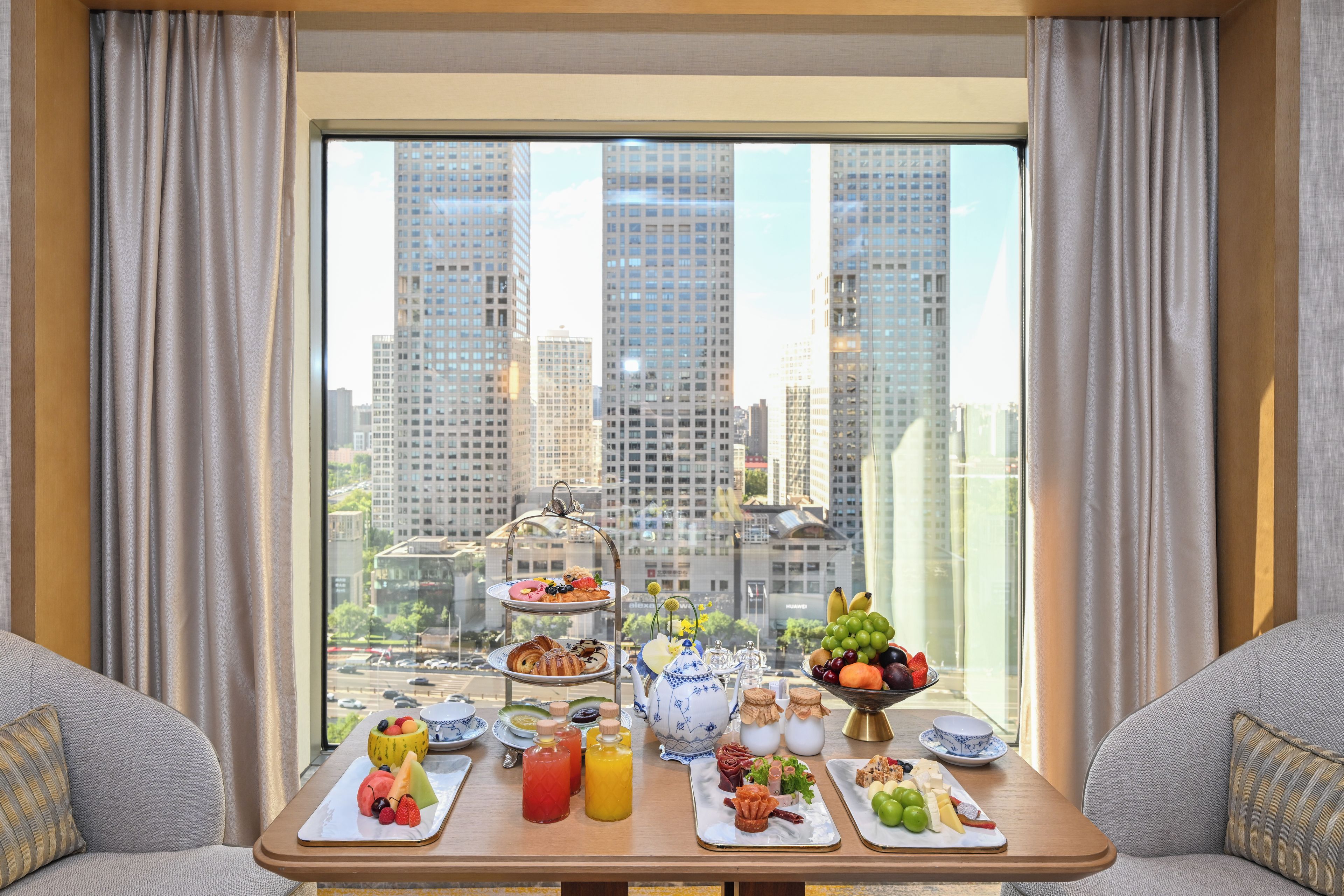 A breakfast table with various food items and a view of tall buildings through a window.