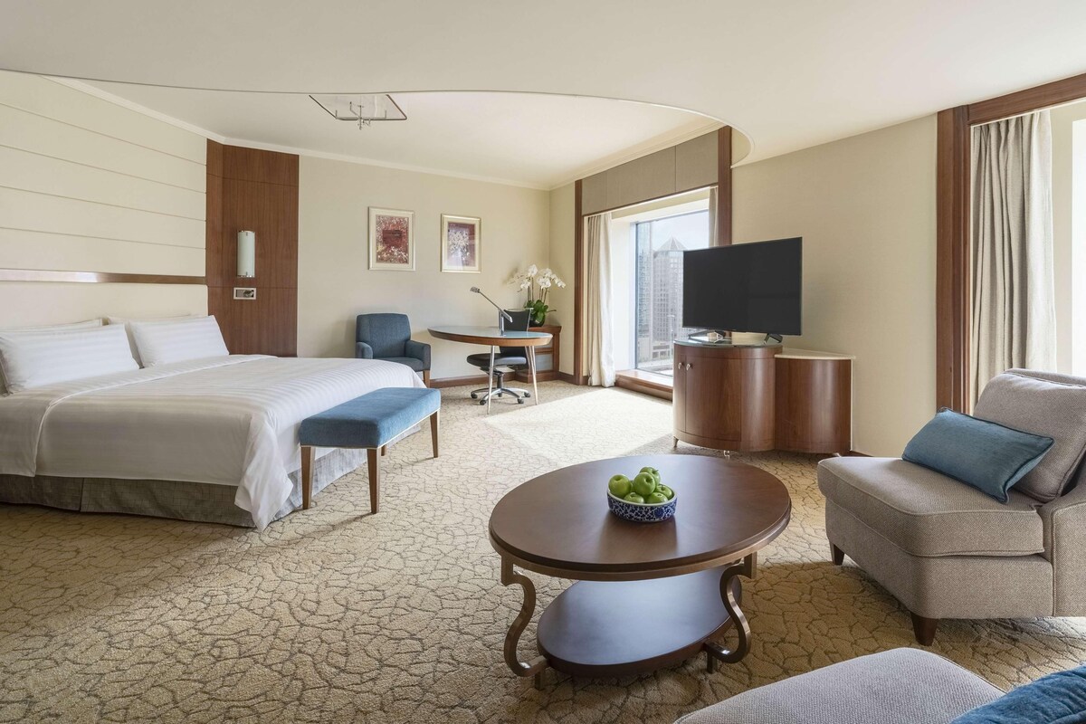 A hotel room with a bed, a desk, a television, and a seating area with a coffee table.