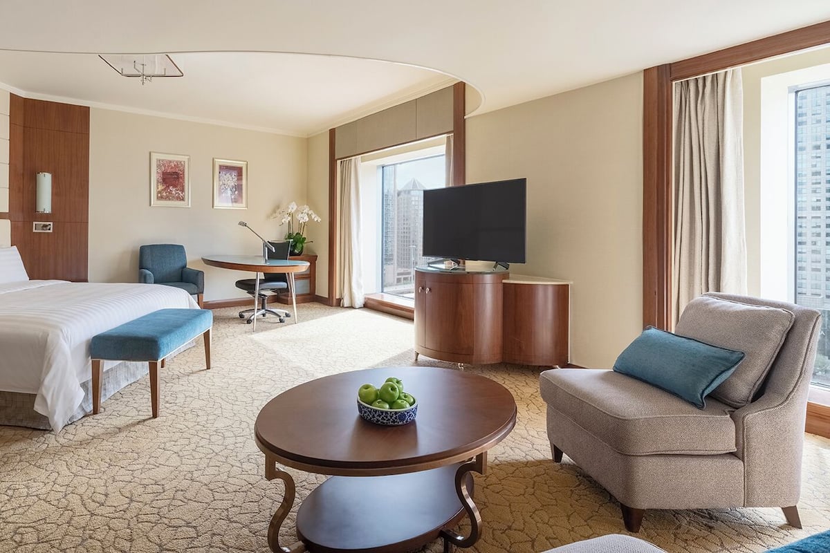 A hotel room with a bed, a desk, a chair, a television, and a view of the city.