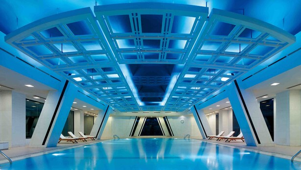Ein moderner, überdachter Pool mit geometrischer Deckenkonstruktion und Liegestühlen am Rand.