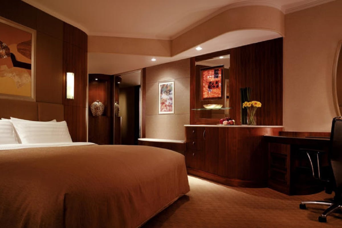 A hotel room with a large bed, a desk, and a chair. There is a mirror above the desk and a painting on the wall.