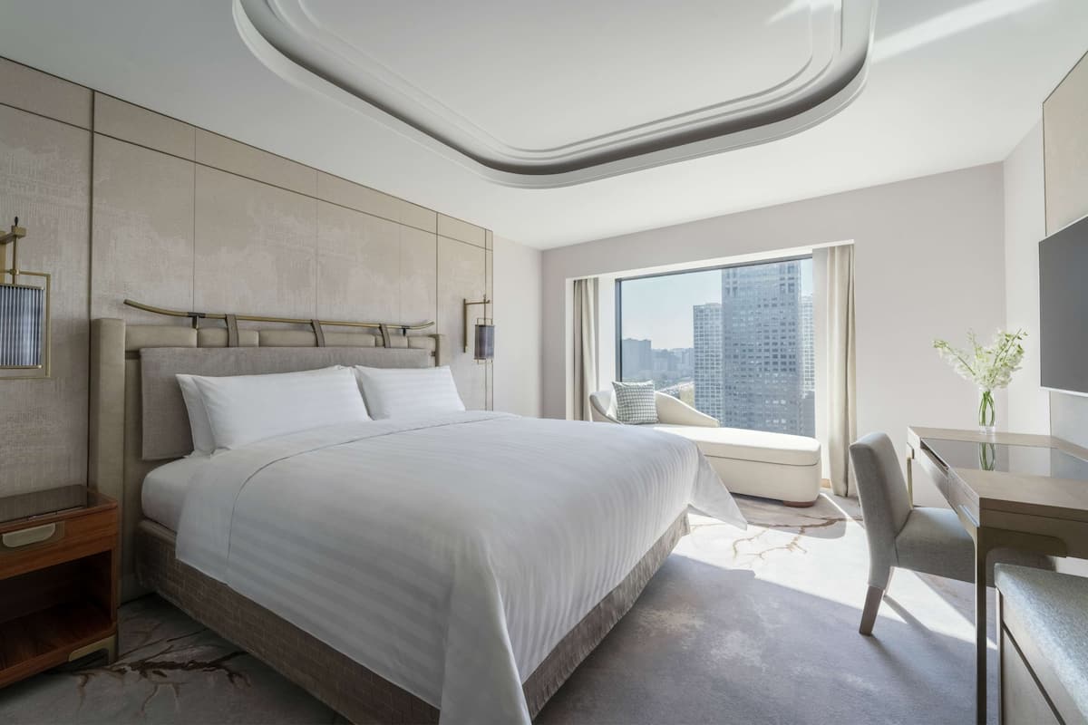 A modern hotel room with a large bed, a desk, and a view of the city.