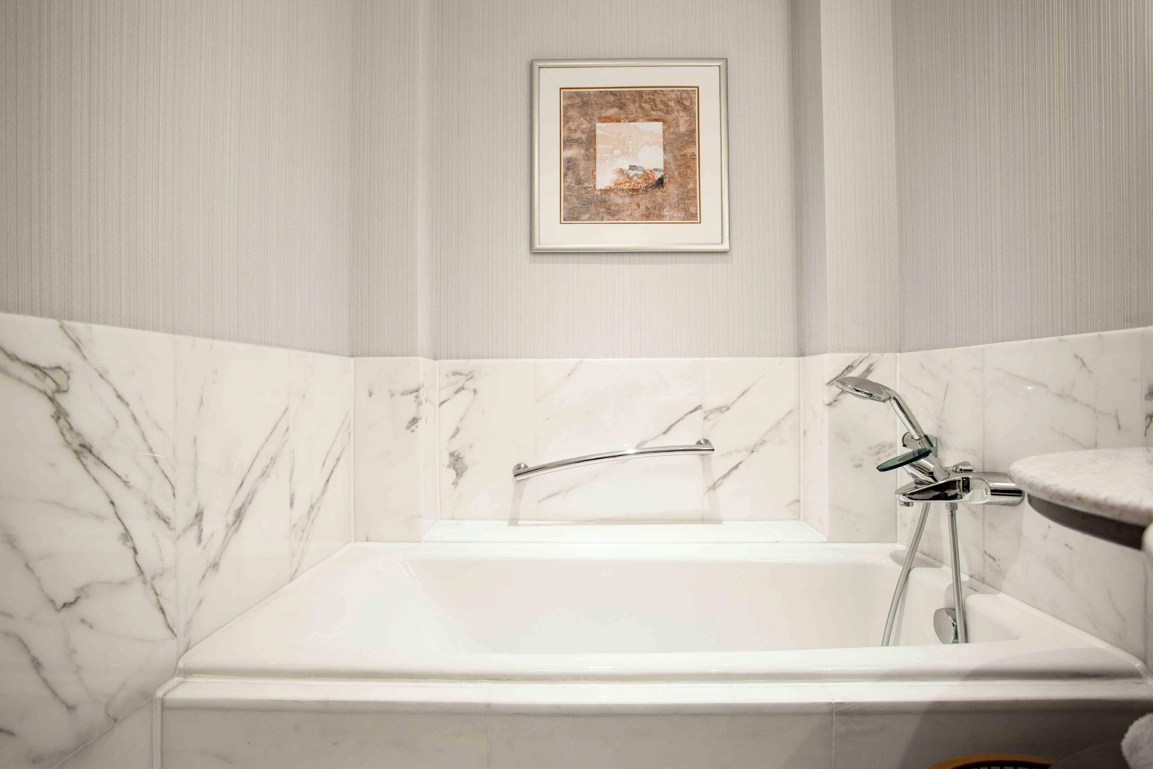 Une salle de bain avec une baignoire blanche, des murs en marbre et un tableau encadré accroché au mur.