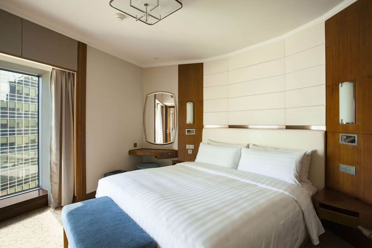 A hotel room with a large bed, a bedside table, a mirror, and a window with curtains.