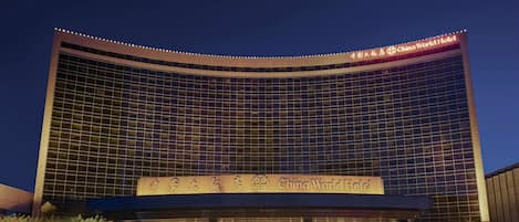 A modern hotel with a curved facade, illuminated signage, and a covered entrance area.