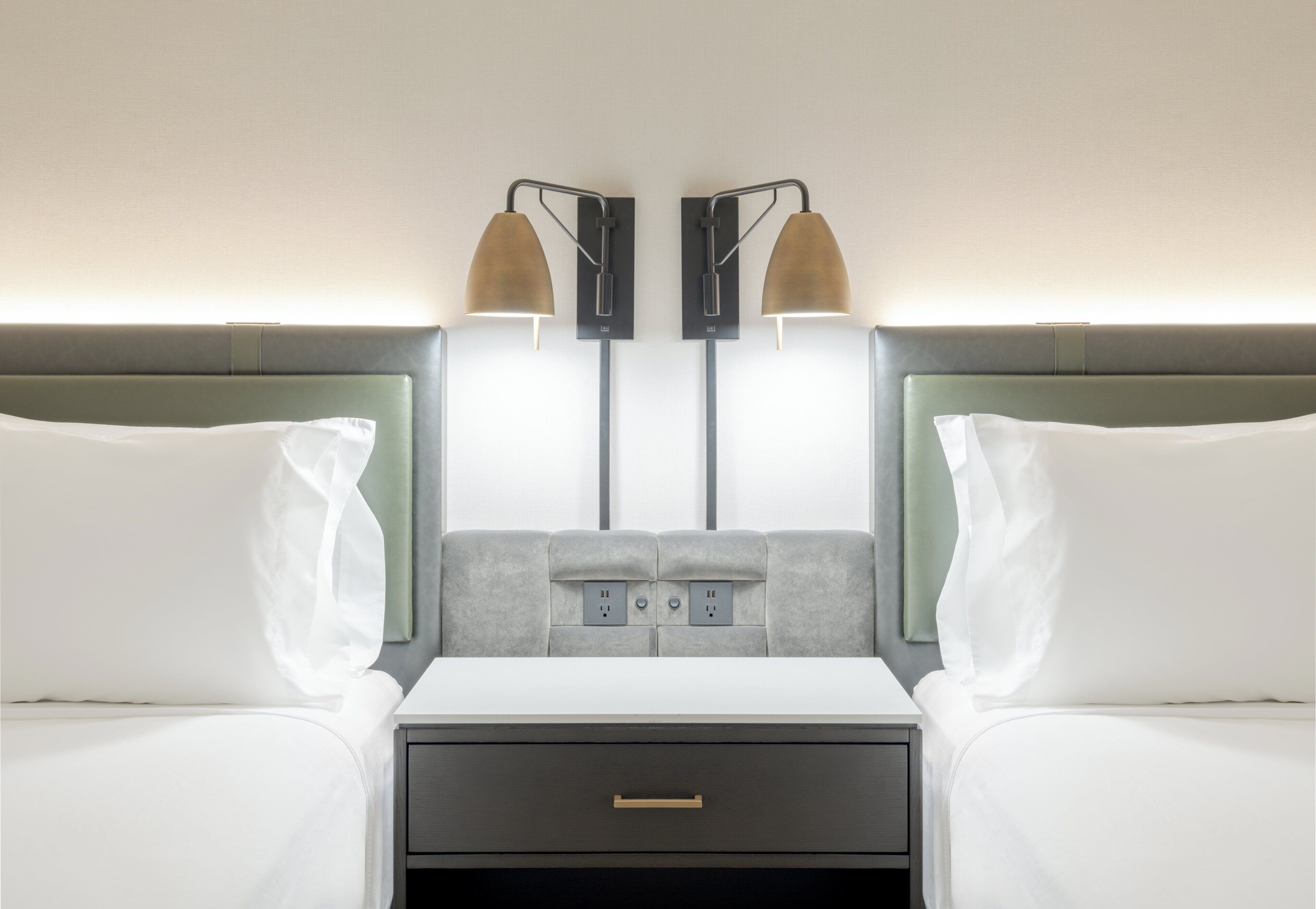 A hotel room with two beds, a nightstand, and a wall-mounted lamp.