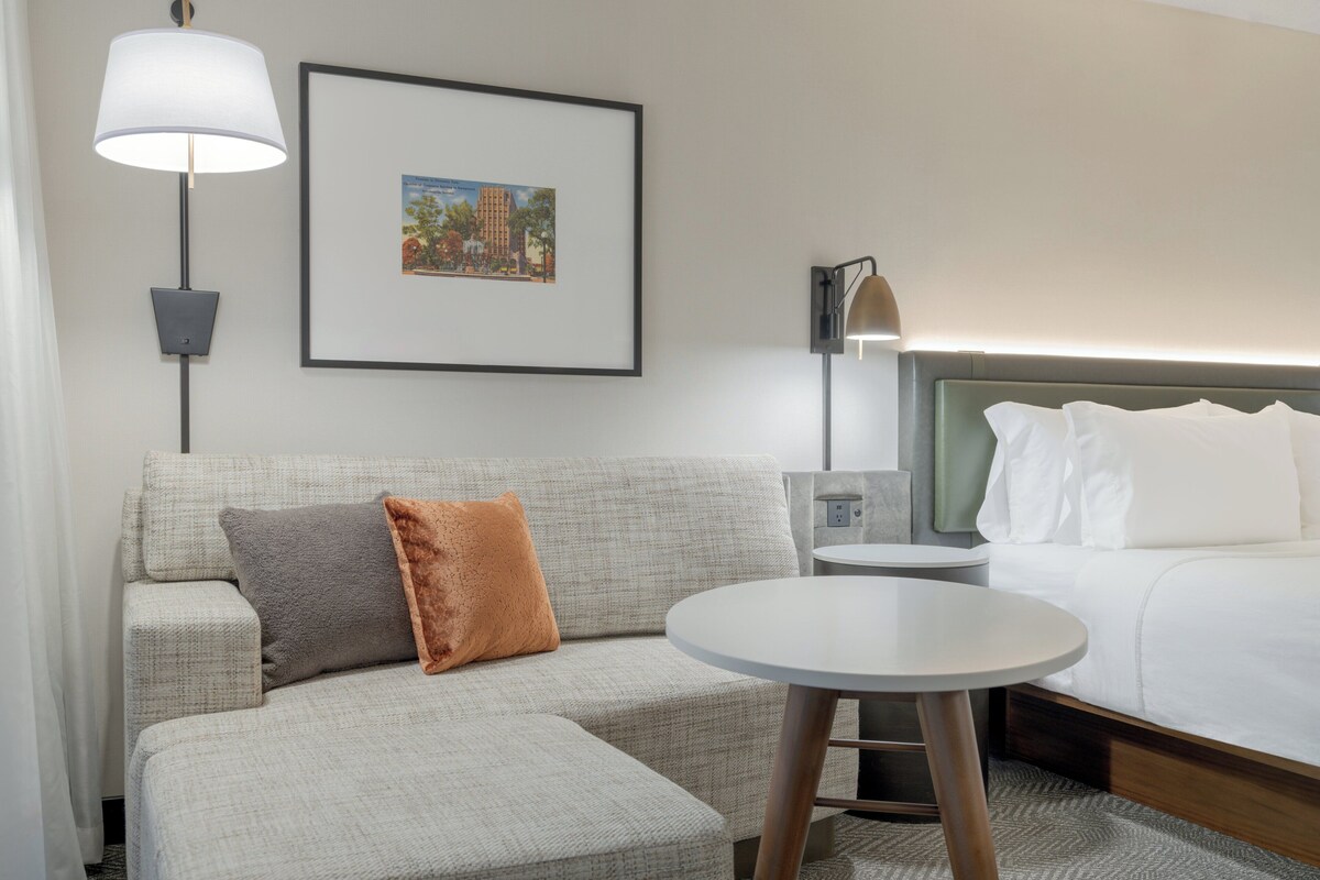 A hotel room with a sofa, a small table, a bed, and two wall-mounted lamps.